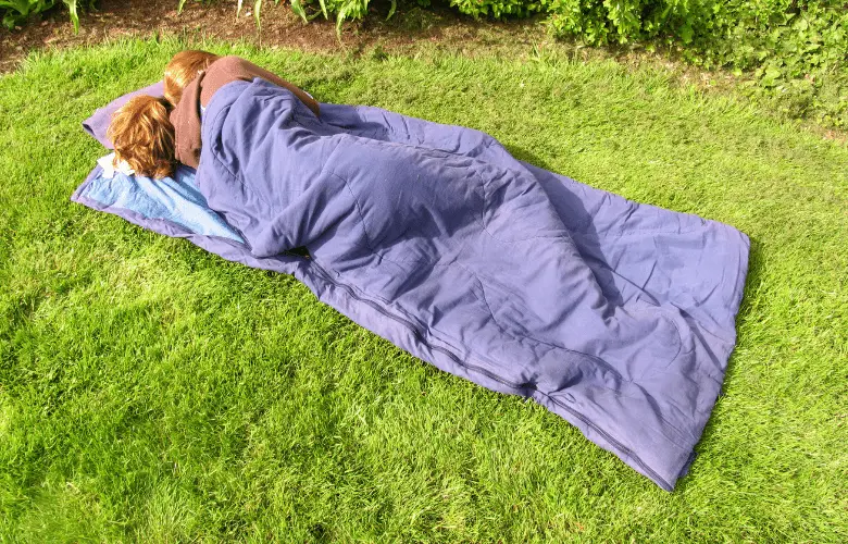 A woman lies on the ground wearing a rectangle sleeping bag