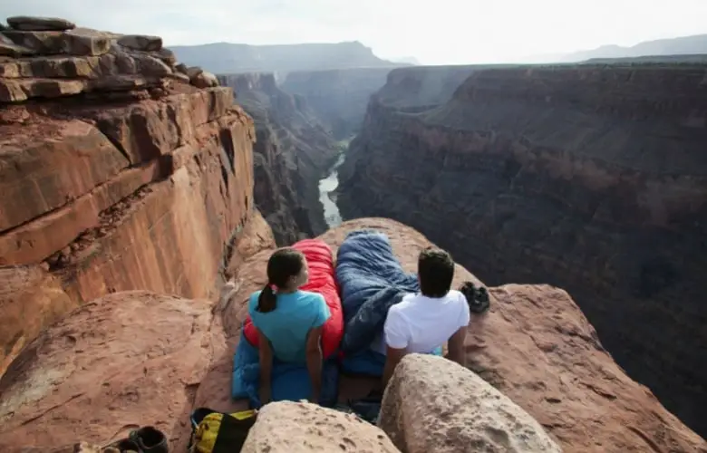 Couple near the edge of a cliff wearing their sleeping bags